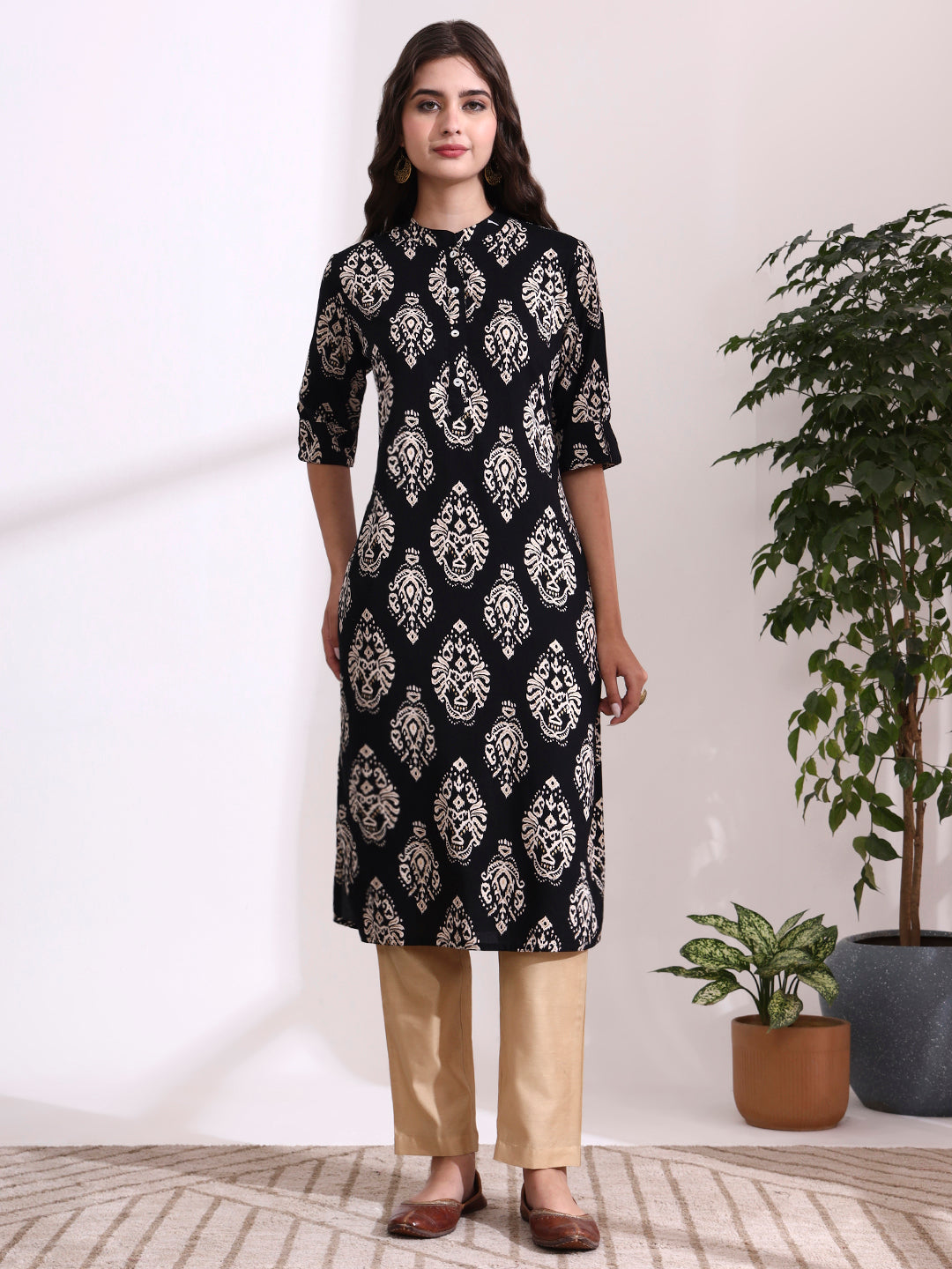 Woman wearing a black patterned kurta with beige pants in a minimalistic room.