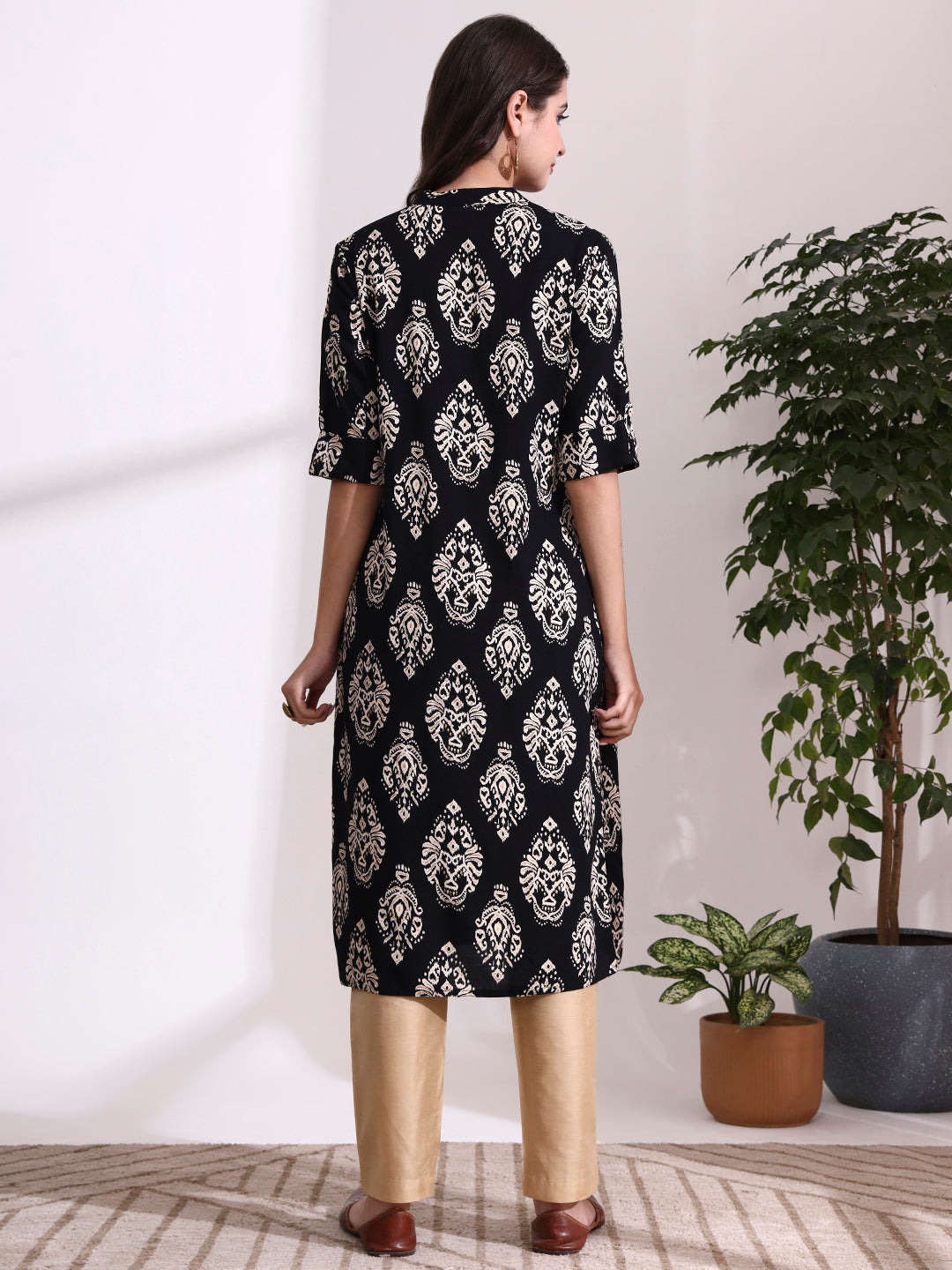 Woman wearing a black and white patterned kurta with beige pants in a minimalistic room.