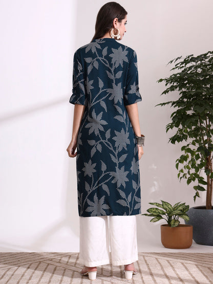 Woman wearing a dark blue floral patterned kurta with white pants in a minimal indoor setting.