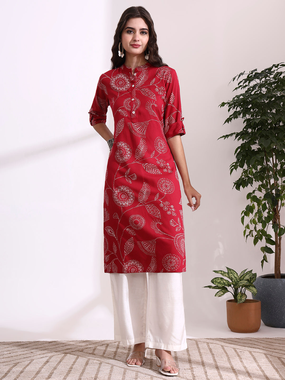Woman wearing a red patterned kurta with white pants in a minimalistic room.