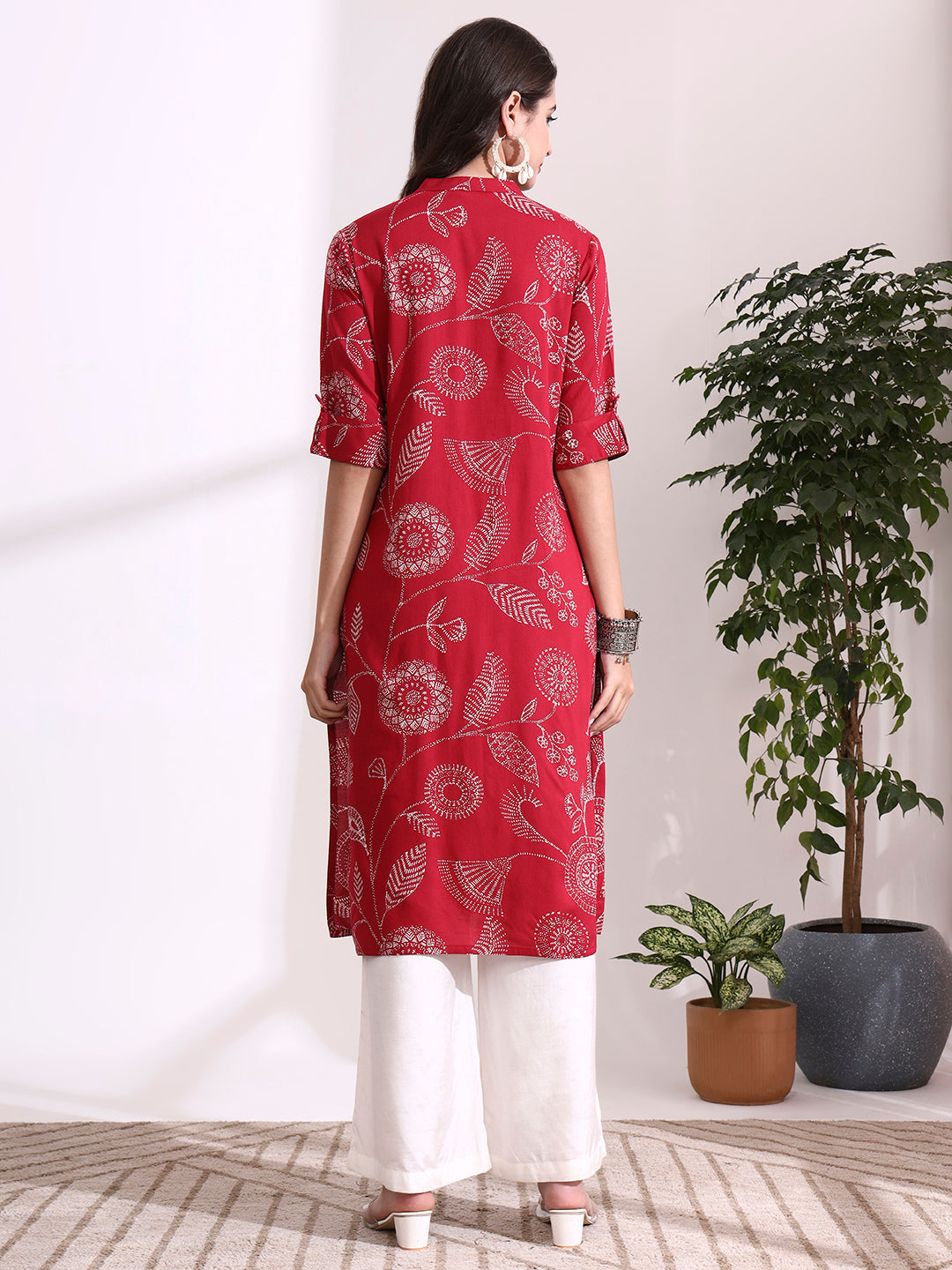 Woman wearing a red floral patterned kurta with white pants in a minimalistic room.