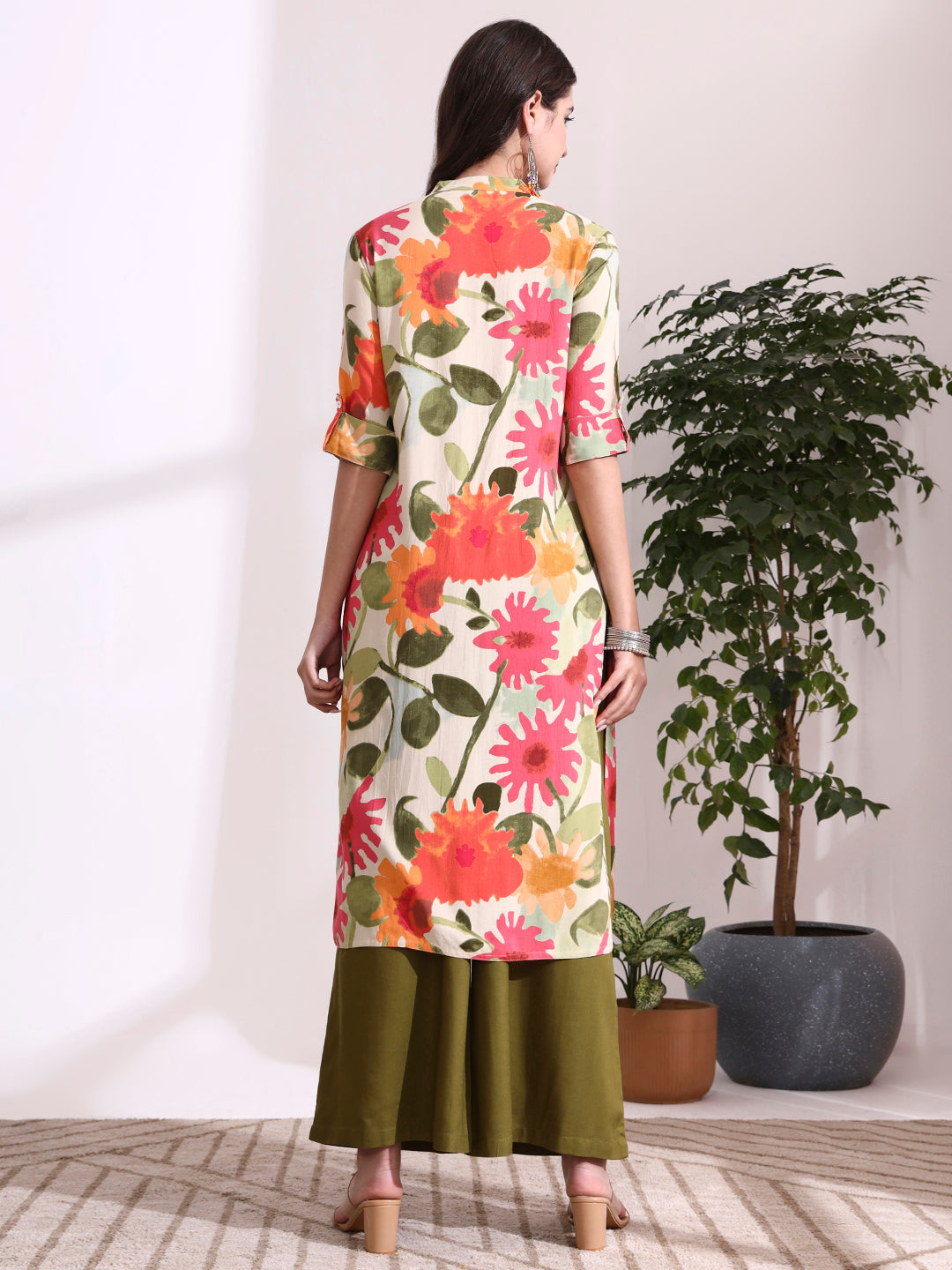 Woman wearing a floral dress standing in a room with plants.