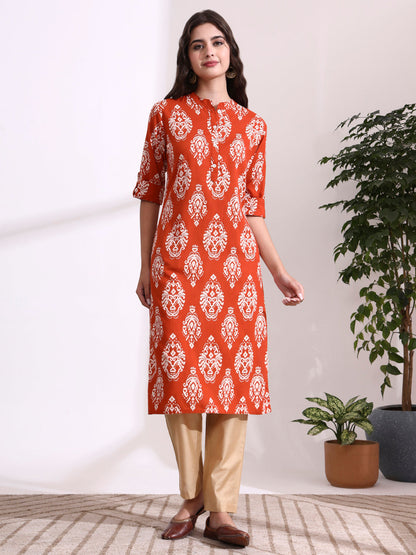 Woman wearing an orange and white patterned kurta with beige pants in a minimalistic setting.