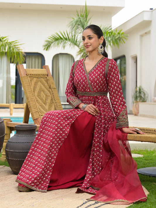 Woman in a red and gold traditional outfit sitting outdoors.