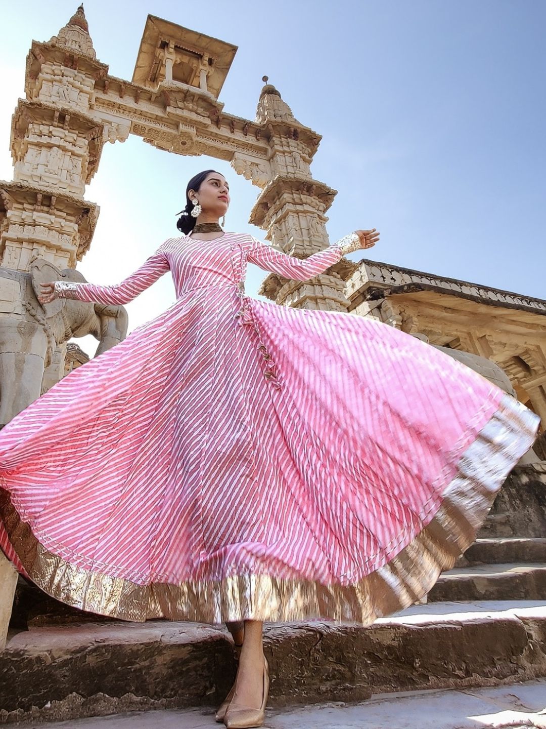 Woman in a pink and gold dress standing in front of a stone archway.
